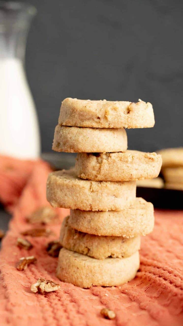 Butter pecan cookies on each other with a glass of milk in the backdrop.