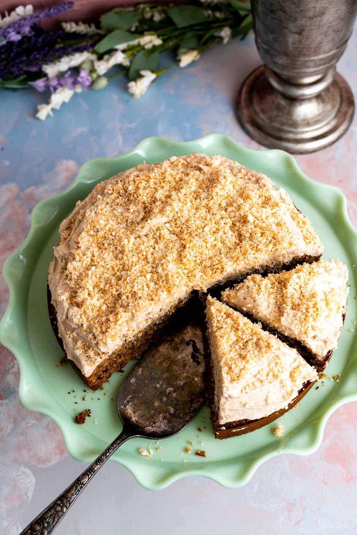 Coconut coffee cake with cut slices sitting on the green color cake plate.