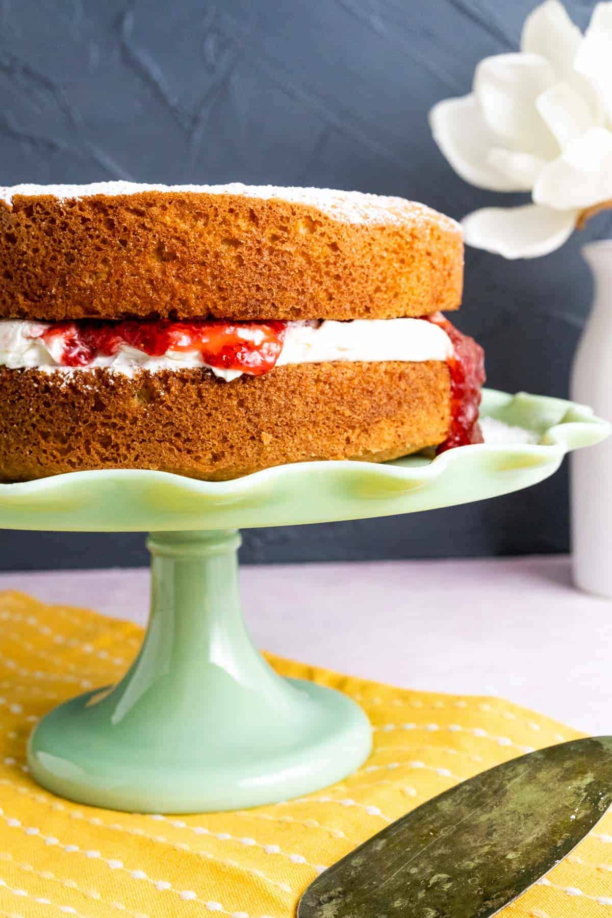 Victoria Sponge Cake placed on a green cake plate with an antique silver spoon on the side.