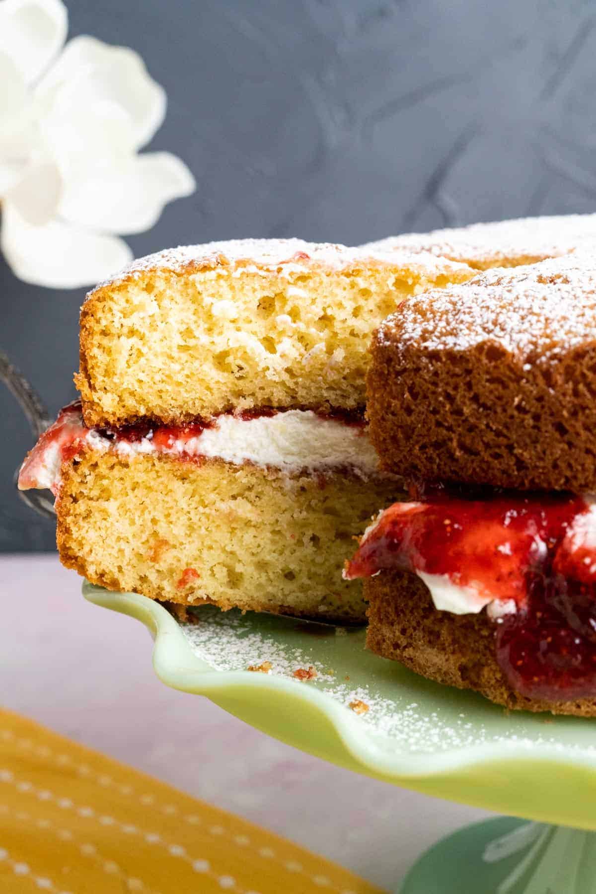 One slice of victoria sponge cake in the cake plate showcasing the cream and jam layer.