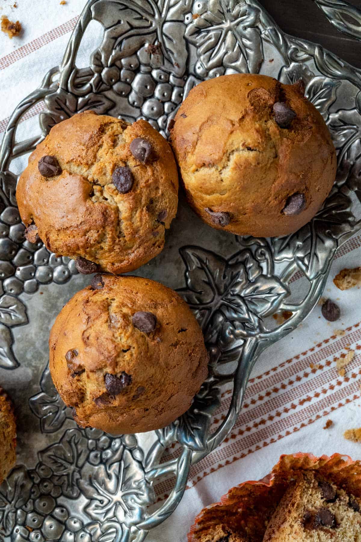 three muffins placed in a carved silver tray with crumbs scattered on the white table cloth.