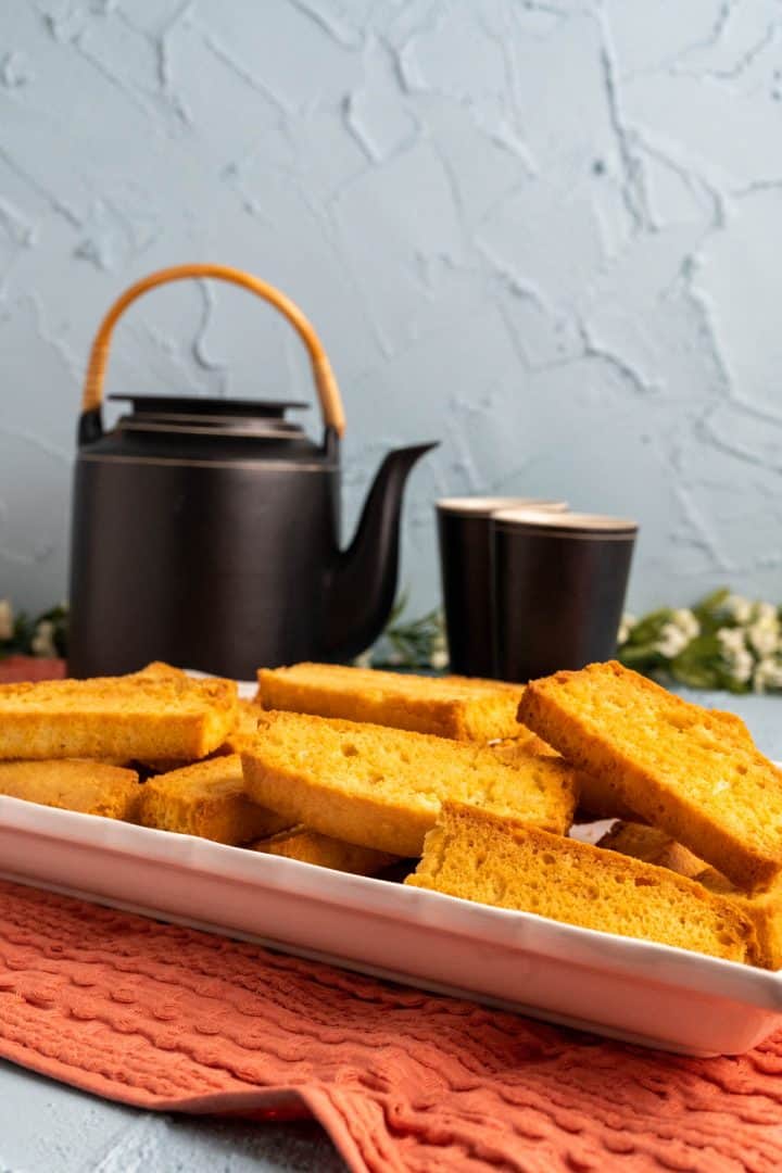 pieces of rusks in a white plate with tea kettle in the backdrop.