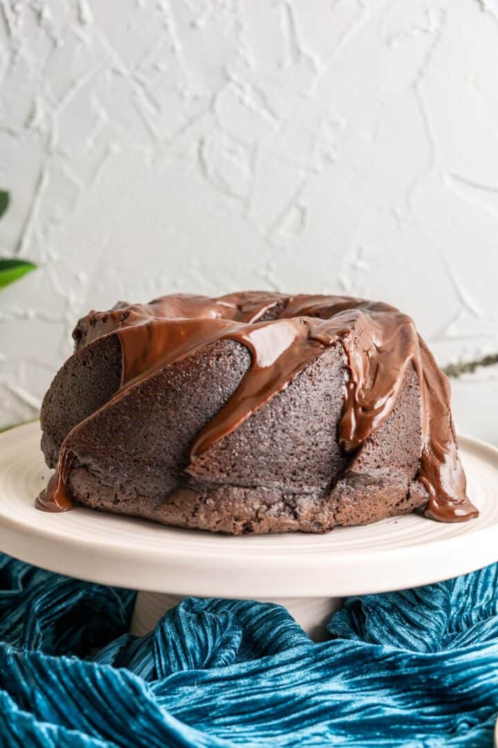 Chocolate cake in the cake plate with ganache running on the side.