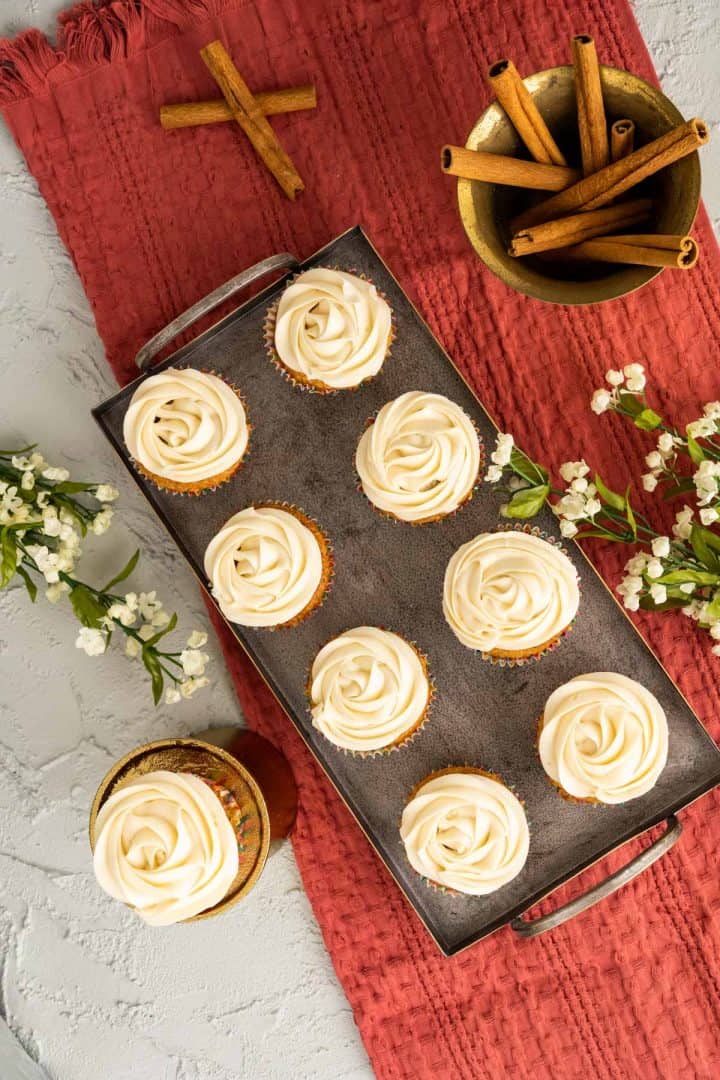 overhead shot of cinnamon cupcakes with cream cheese frosting on a silver tray. 