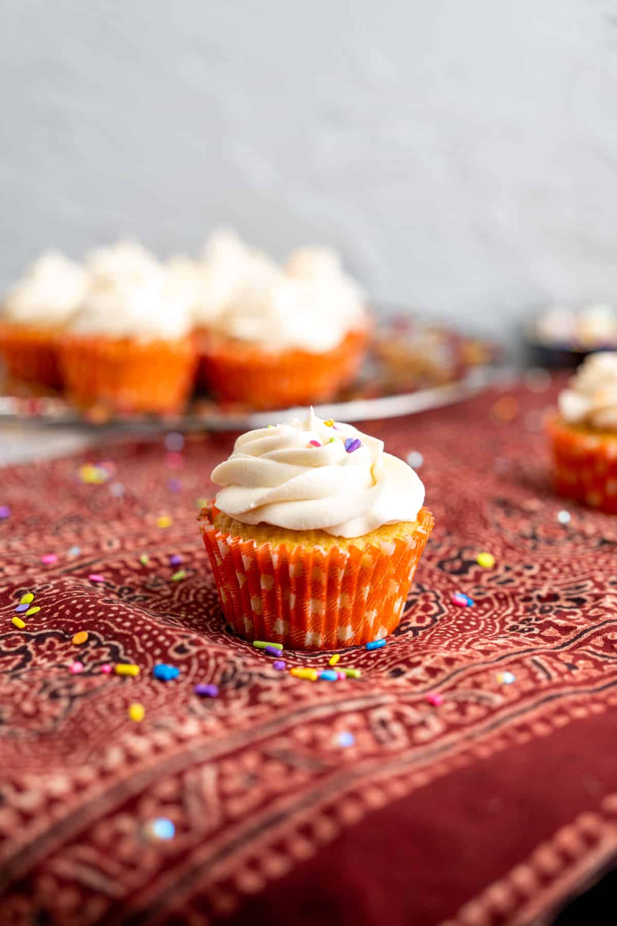 single vanilla cupcake topped with butter cream frosting on a red table cloth.