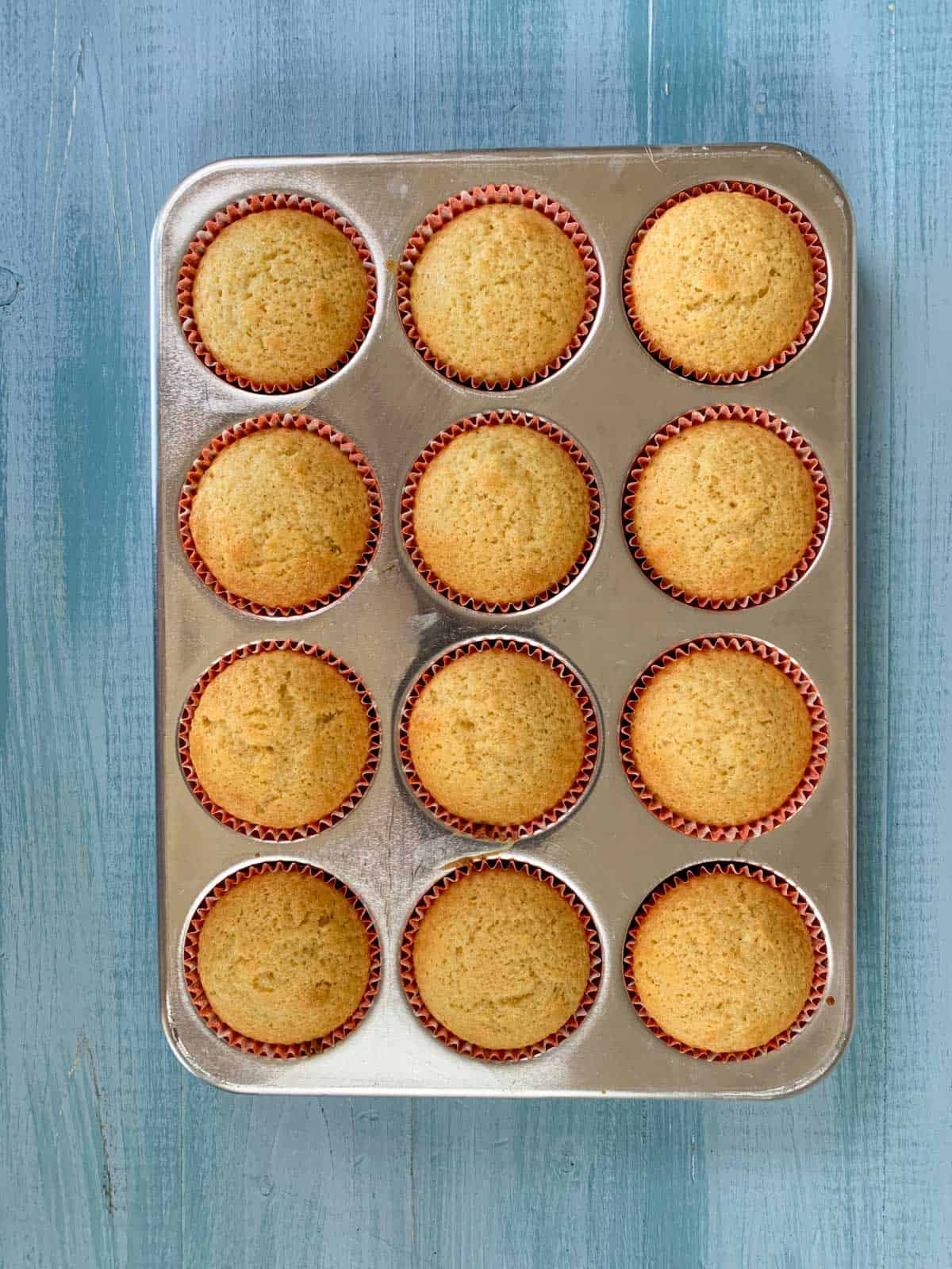 baked vanilla cupcakes with oil in a muffin tray on a blue table. 