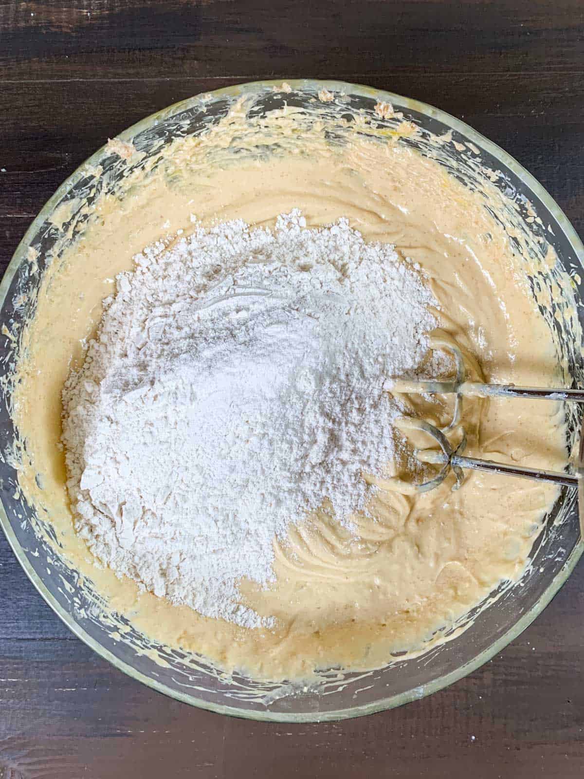 adding dry ingredients to the wet ingredients to prepare peach cobbler pound cake batter.