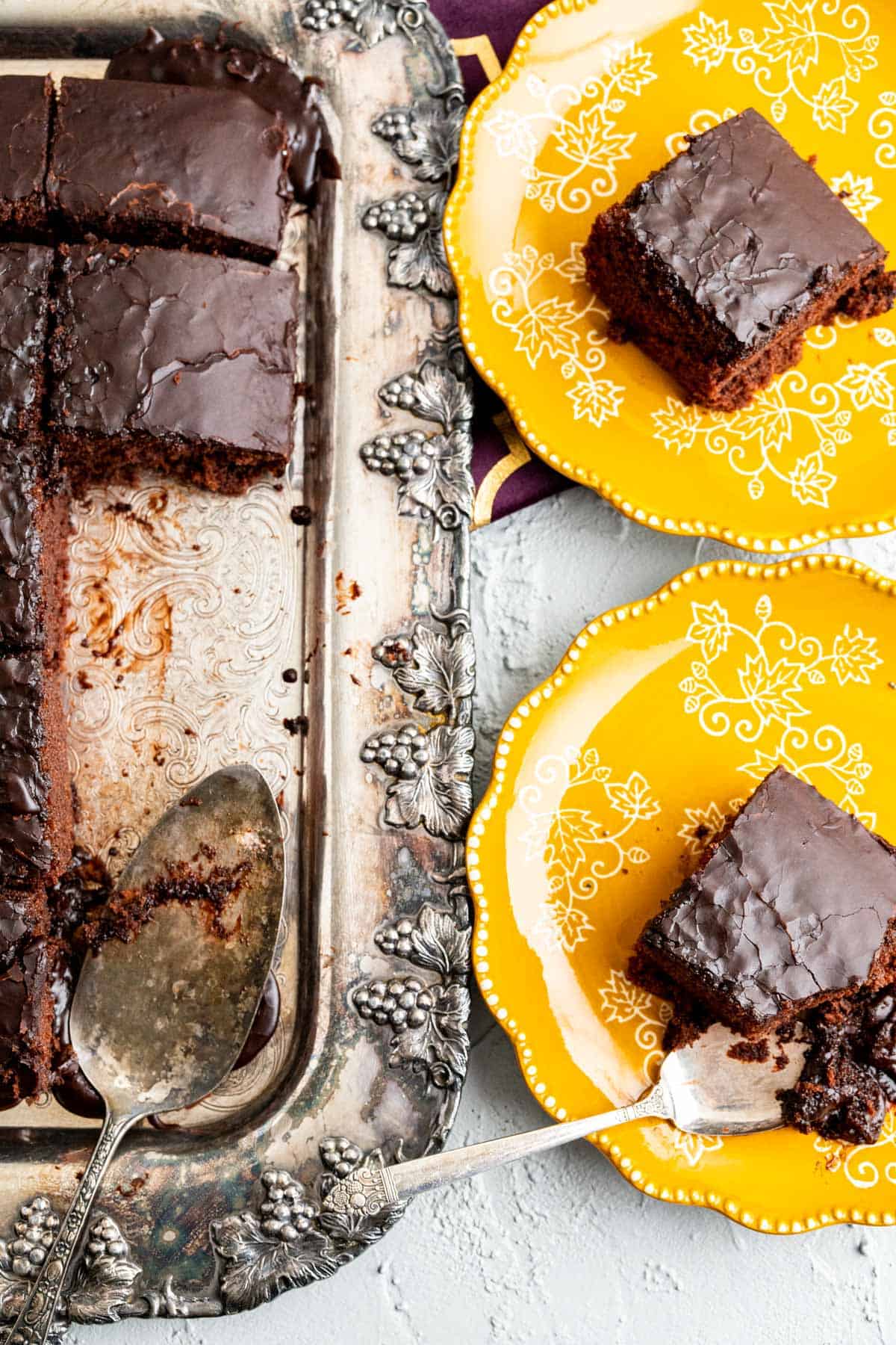 overhead shot of coca cola cake in a silver tray with two yellow plates on the side with cake pieces.