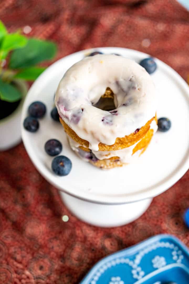 close shot of the donut with blueberries scattered on the white plate.