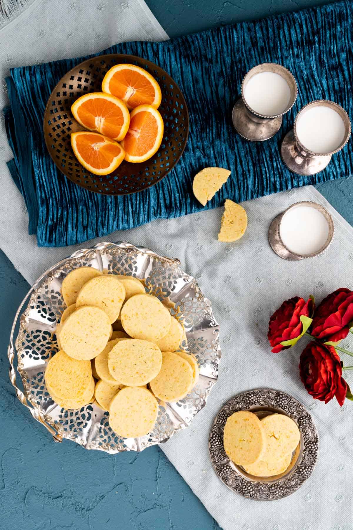 Orange cookies with milk glasses and orange pieces around on the table.