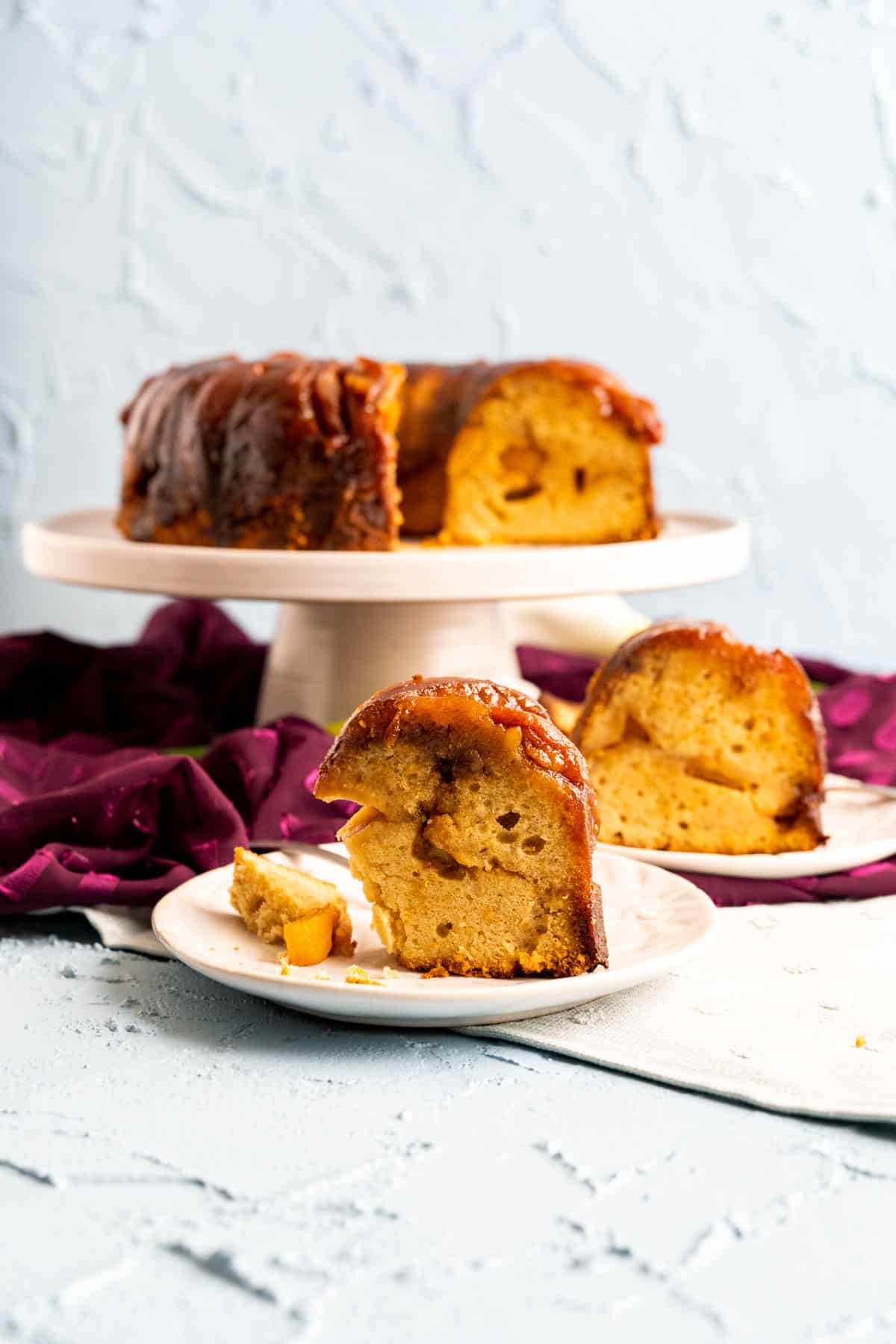 peach cobbler pound cake slices on two white plates with cake in the backdrop.