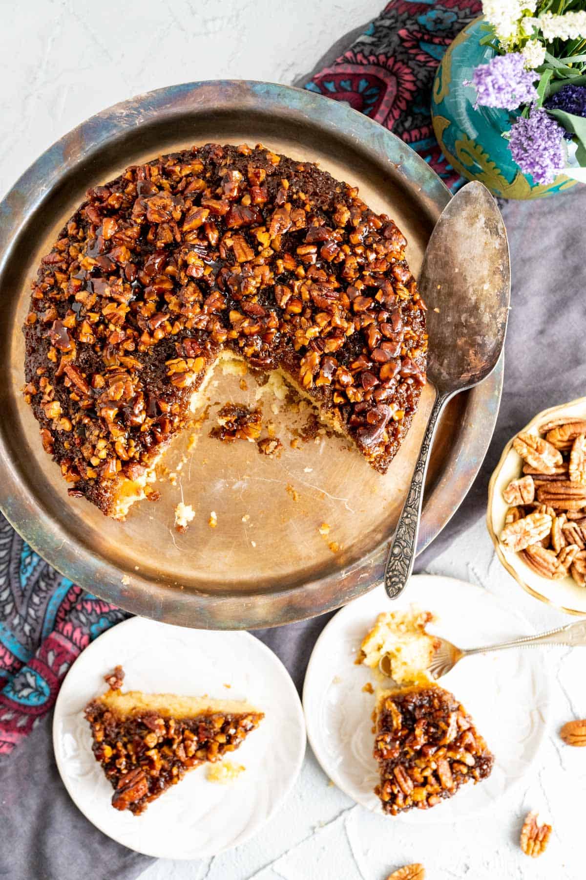 Pecan cake sitting in an antique cake plate along with a silver spoon. 