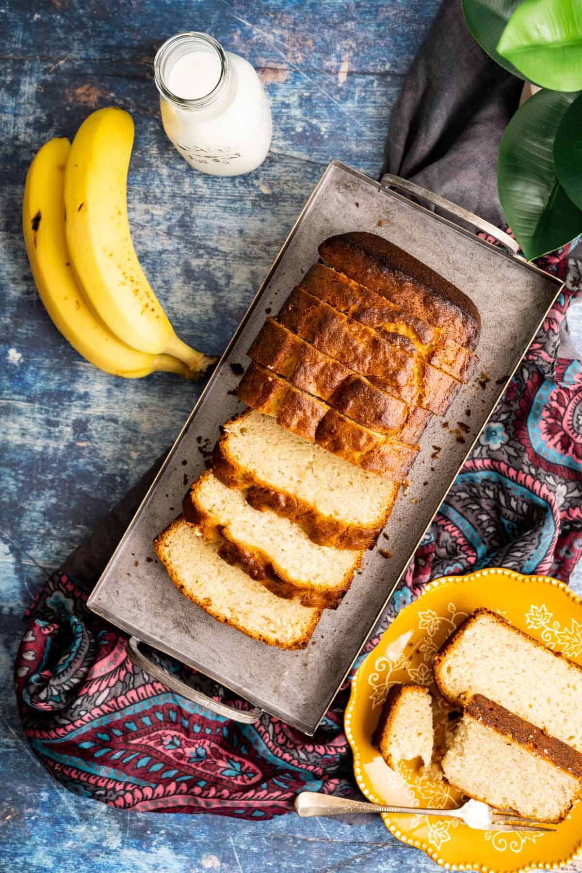 overhead shot of the 4-ingredient banana bread in a silver tray with bottle milk and yellow plates around.