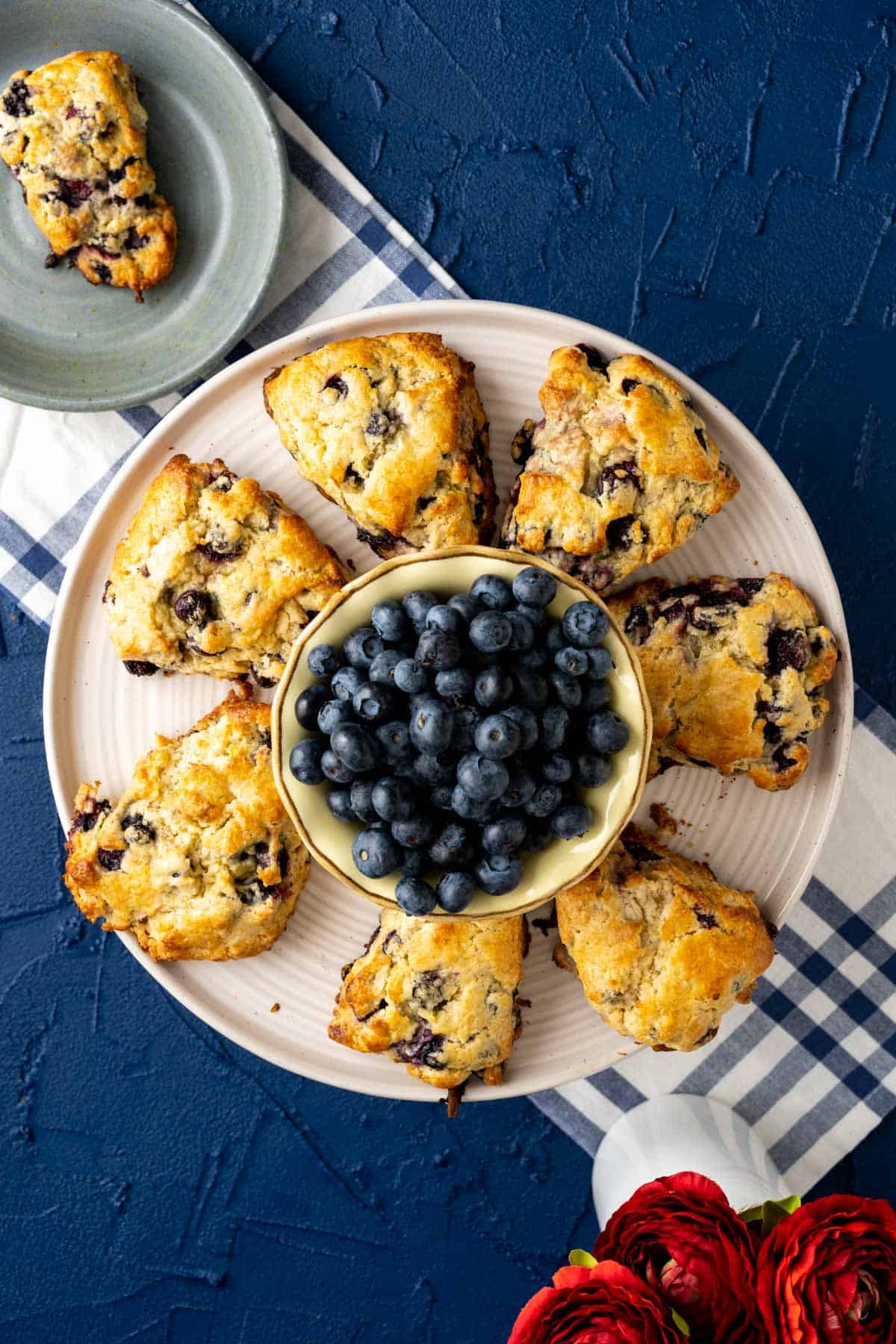 over head shot of the starbucks blueberry scones with blueberries placed in a yellow bowl in the middle of the cake plate.