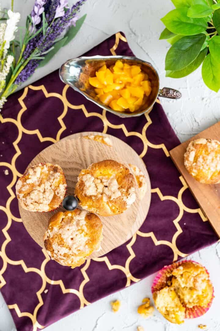 over the head shot of the peach cobbler muffins on the table with purple tablecloth.