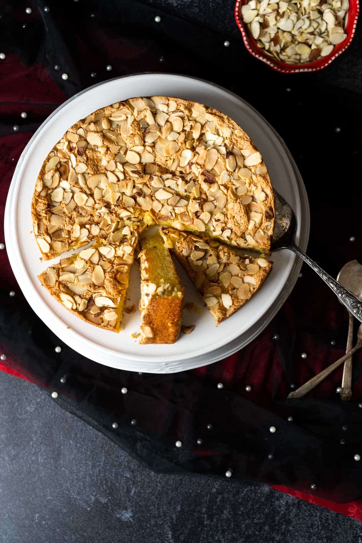 Italian Almond Cake in a white cake plate placed over black table cloth.