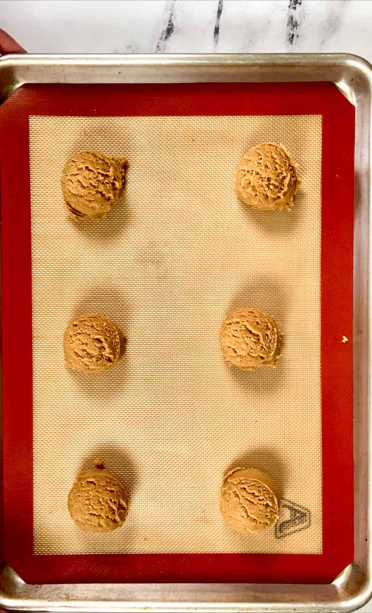 Peanut butter cookies scooped out on a silicone sheet in a baking tray.