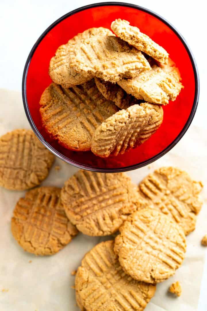 over the head shot of the almond flour peanut butter cookies in a red bowl and some scattered around the bowl.