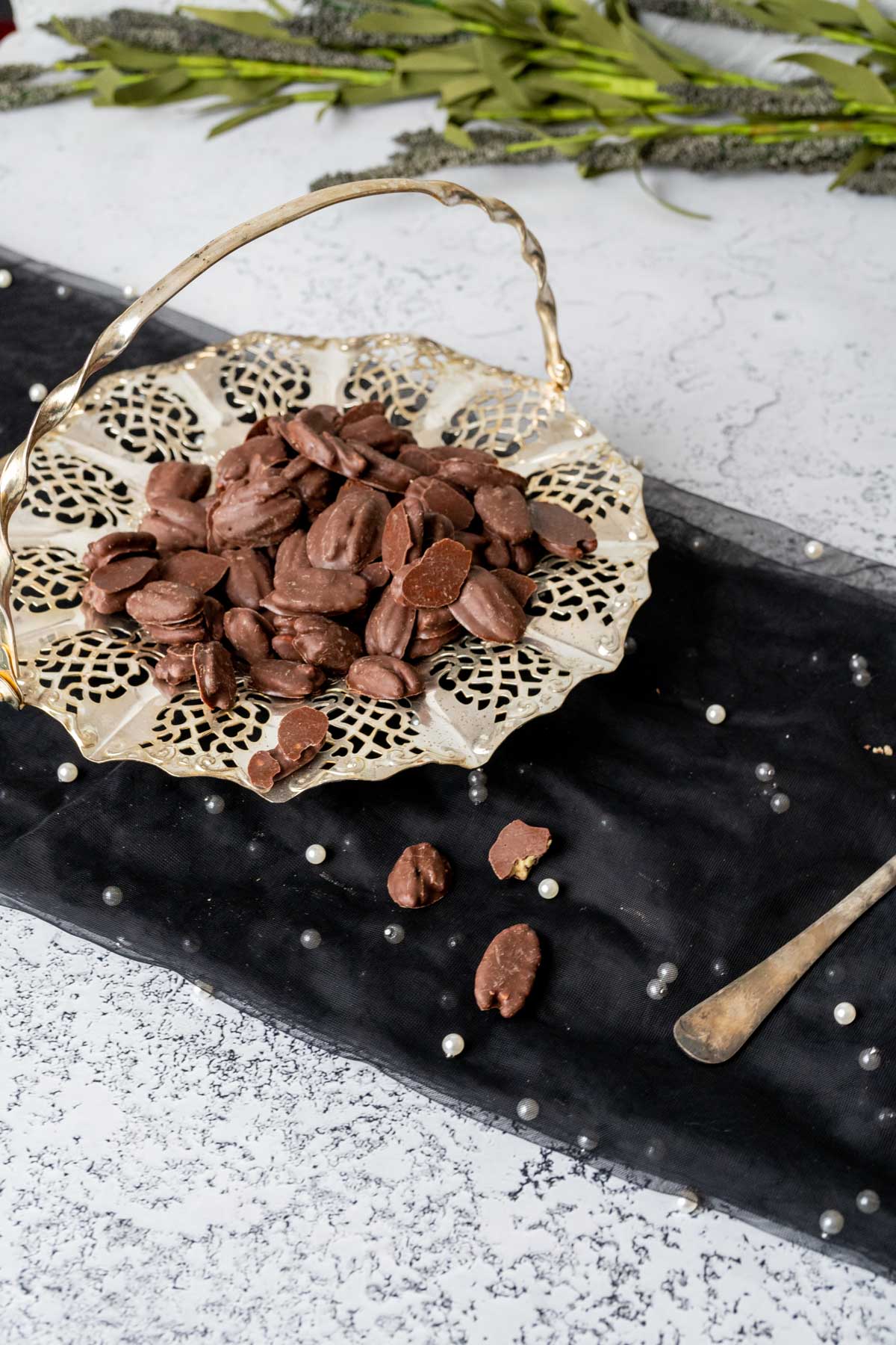 chocolate covered pecans placed in a decorative silver plate with green and black flowers in the backdrop.