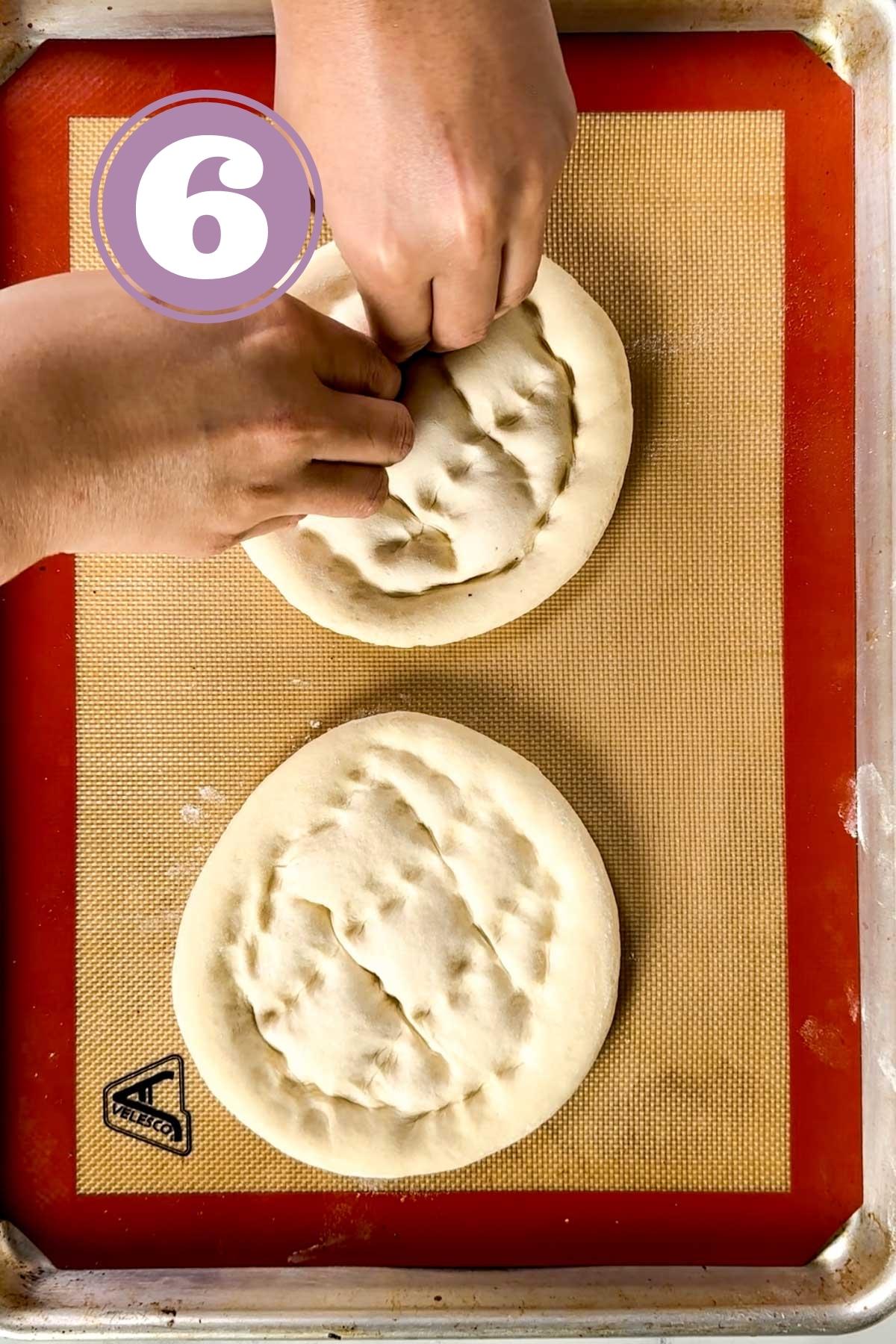 making dents using fingers onto two turkish bread loves sitting on the baking tray.