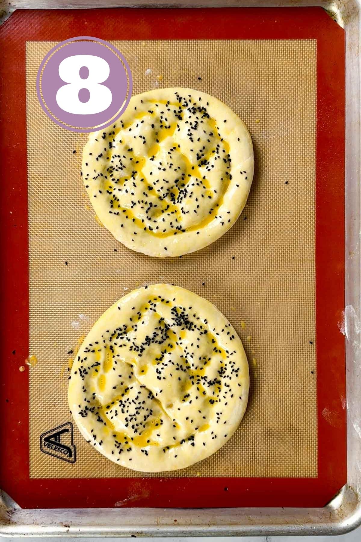 two turkish bread loaves sprinkled with black seeds placed on a silicone mat ready to go to the oven.