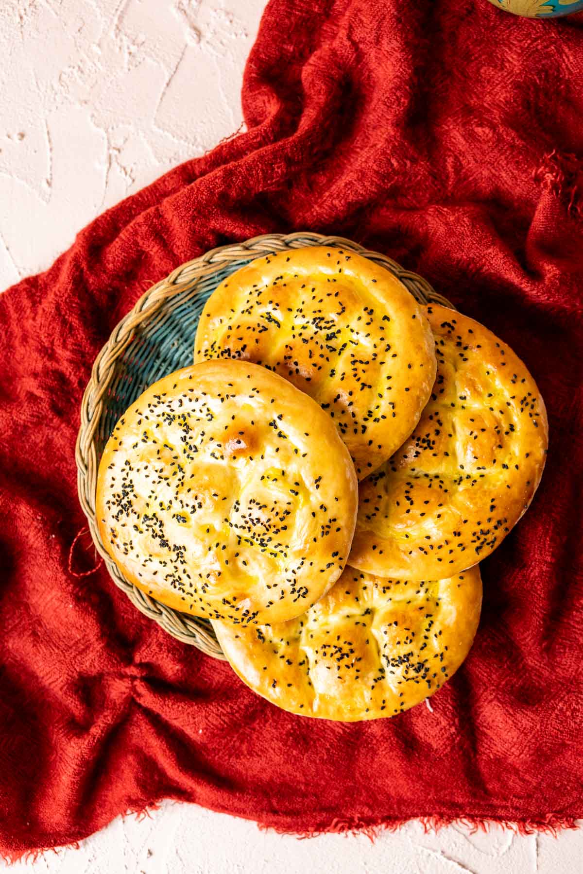 Four Turkish Bread loaves placed side by side in a green basket plate on a red table cloth. 