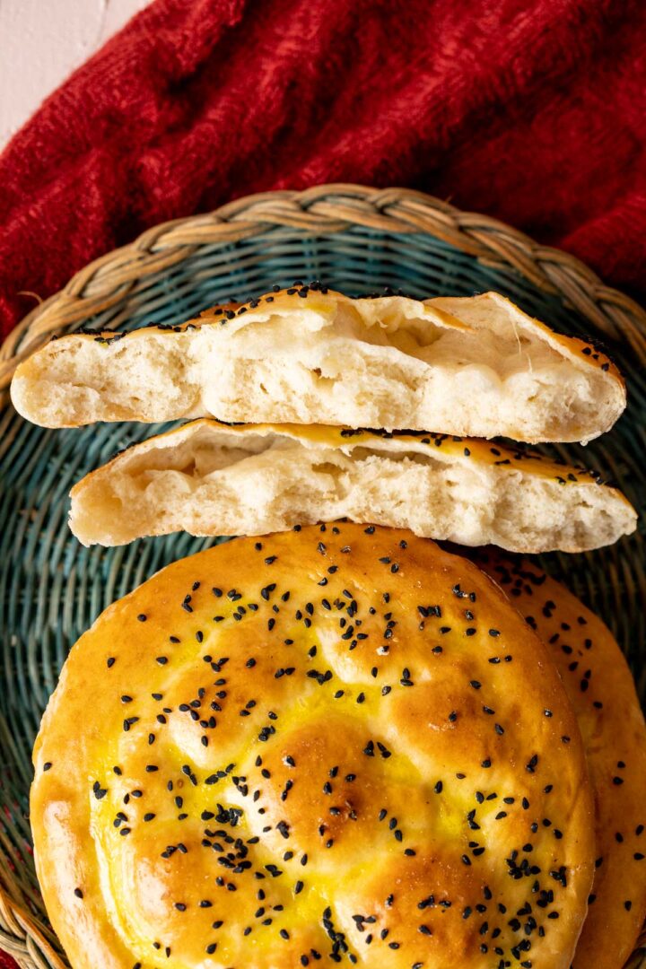 turkish bread loaves with black seeds sprinkled on them placed on a basket plate.