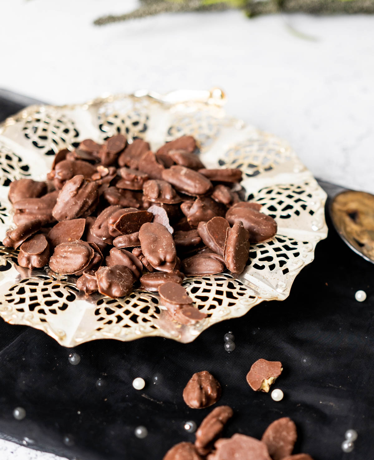 chocolate covered pecans placed in a silver plate on black table cloth with a golden spoon in the side.