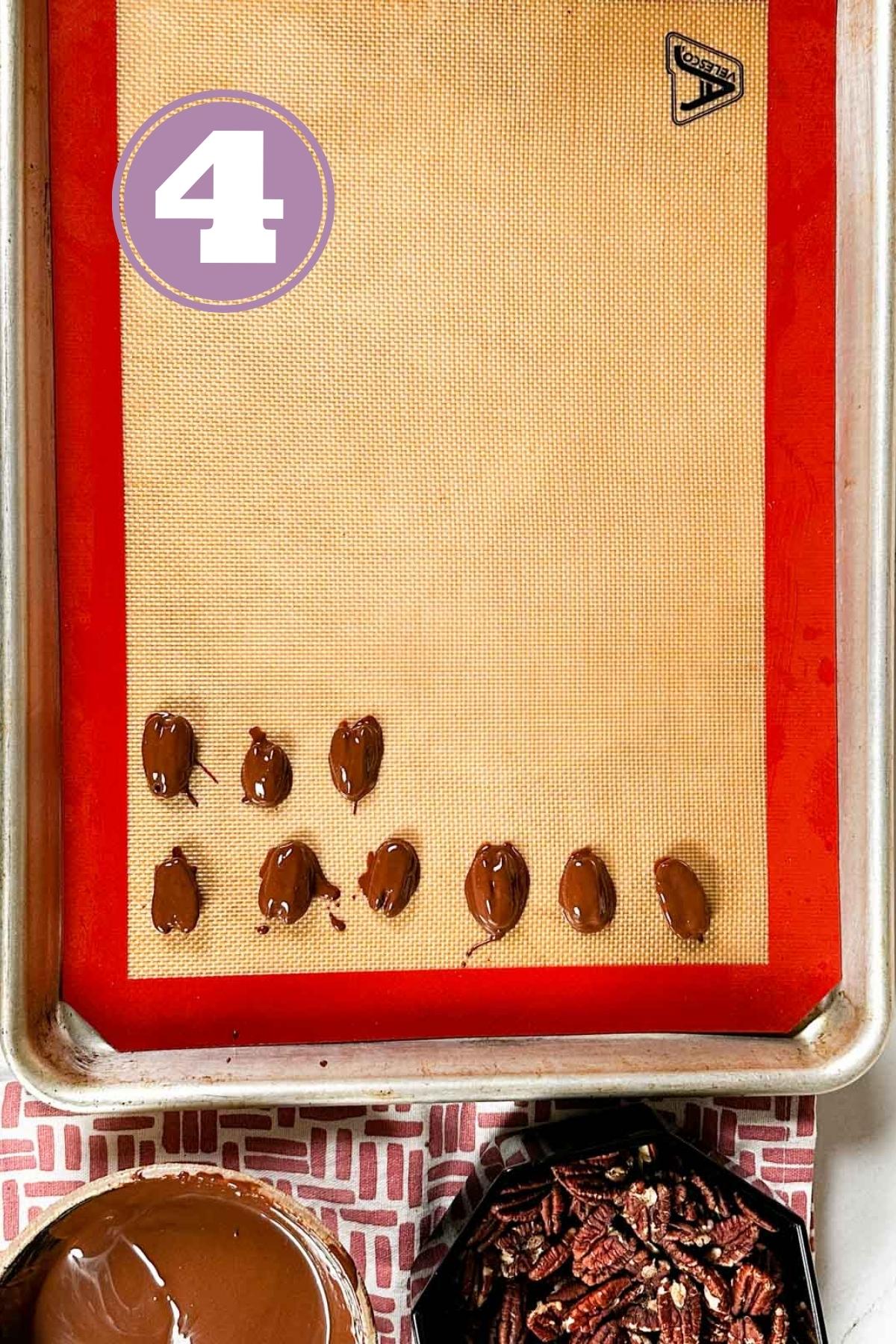 pecans covered in chocolate placed on silicone mat in a baking tray.