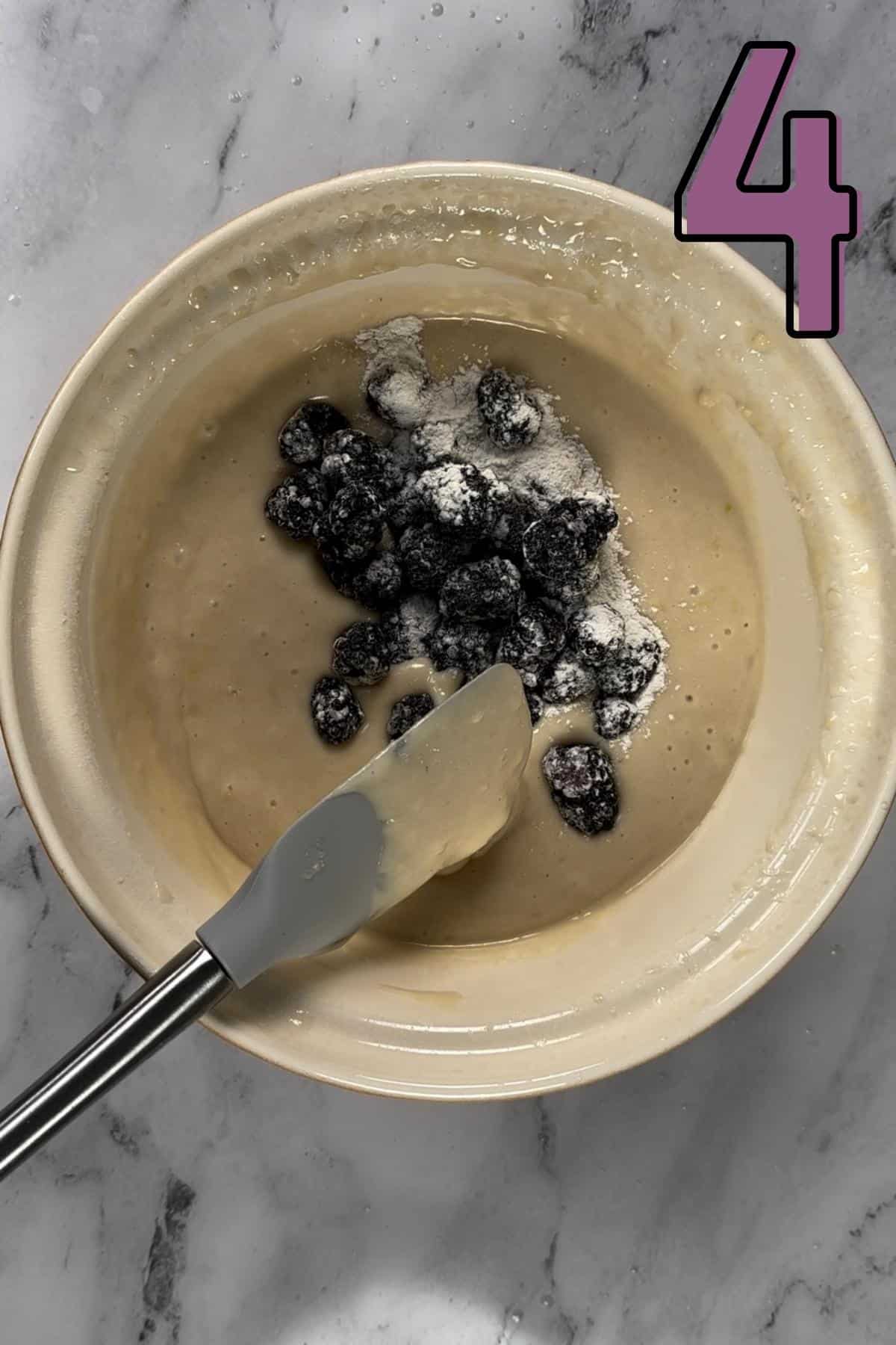 Folding blackberries into the muffin batter using a spatula.