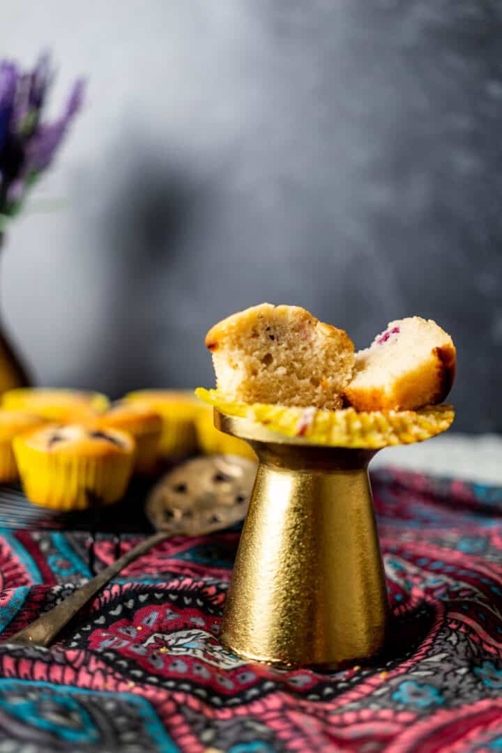 one vegan blackberry muffin sitting on a small and beautiful golden stand with more muffins in the background.