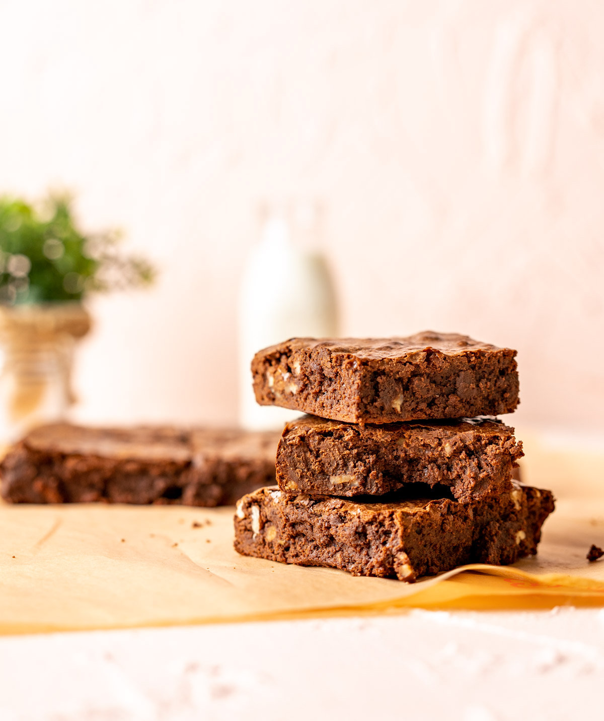 Three overlapped brownies sitting on a brown paper with milk bottle in the back drop.