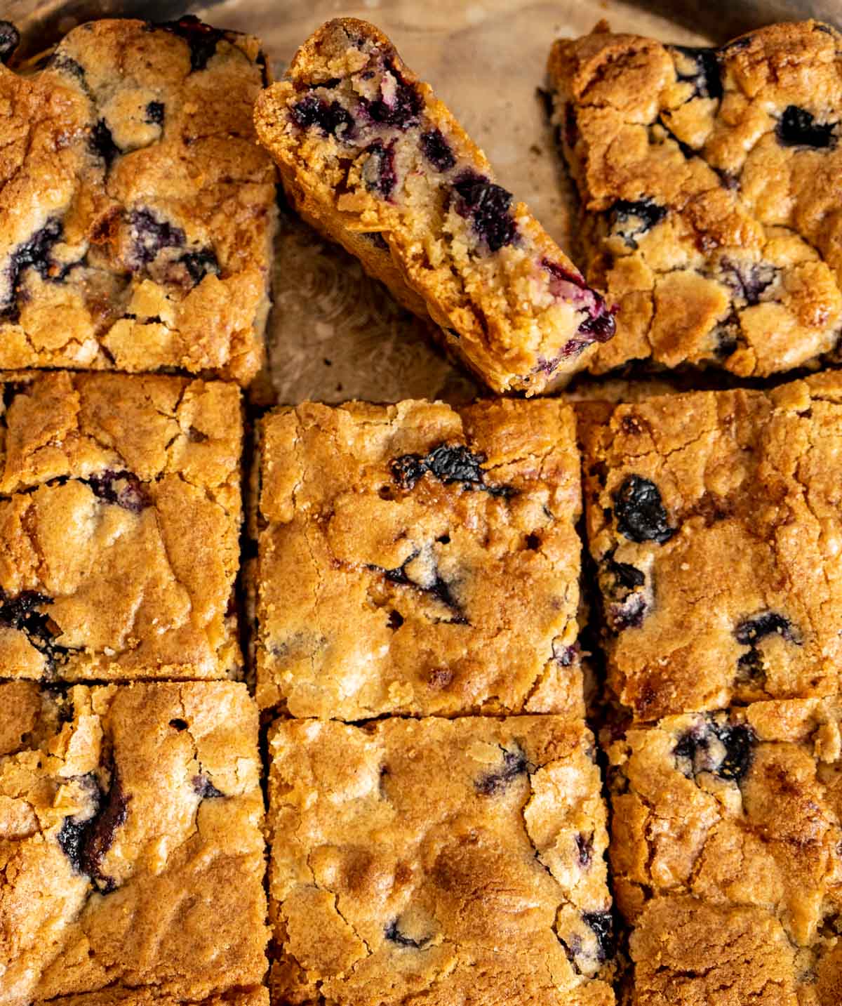 one piece of blueberry blondie standing diagonally among other blondies and showcasing the oozing out blueberries.