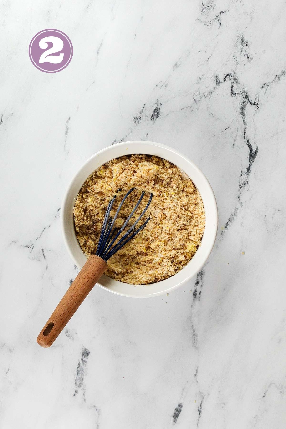 Brown sugar and white sugar with a whisk mixed with lemon zest in a small bowl.