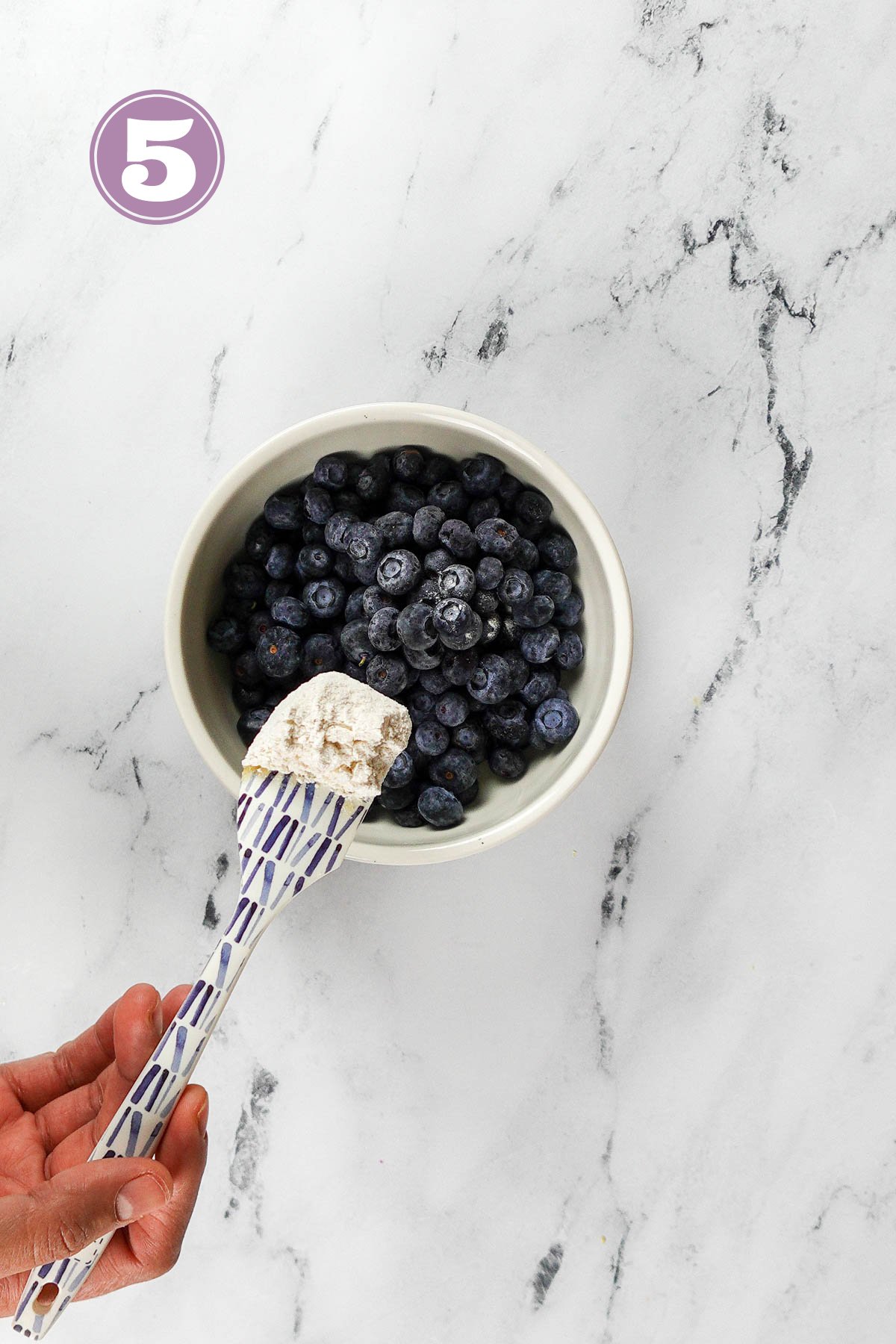 Tossing one tablespoon of all purpose flour into one cup of blueberries.