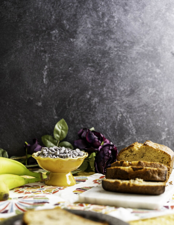 banana bread on a white slab with bananas around on the table.