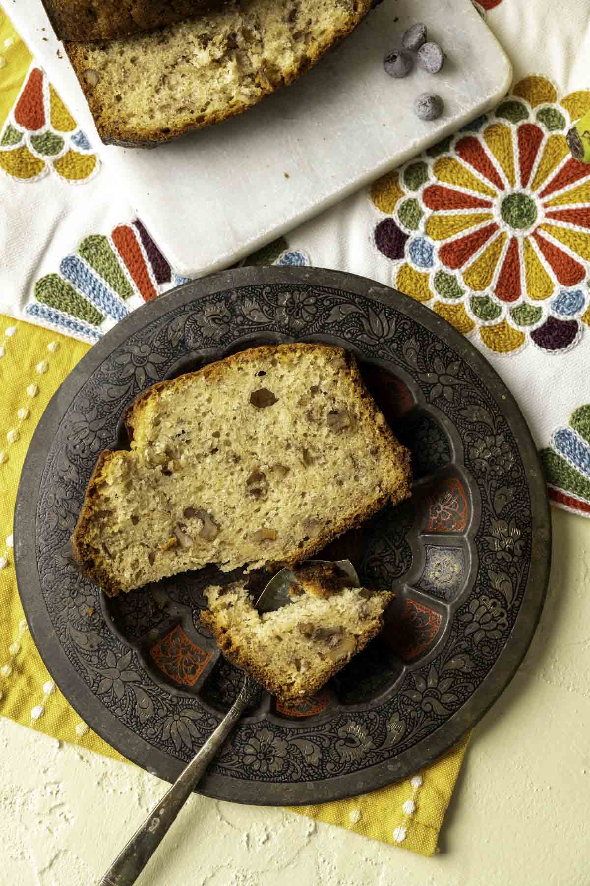 a slice of banana bread placed on a decorative and antique brown plate with an antique spoon.