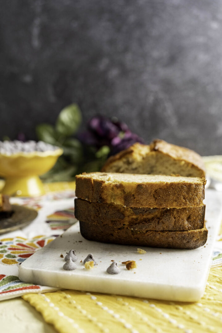 three slices of banana bread on a white marble slab with flowers in the backdrop.