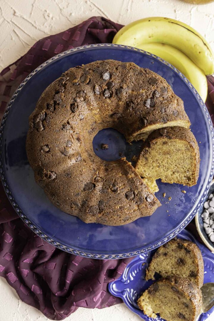 overhead shot of banana chocolate cake on the cake plate with bananas sitting on the table.