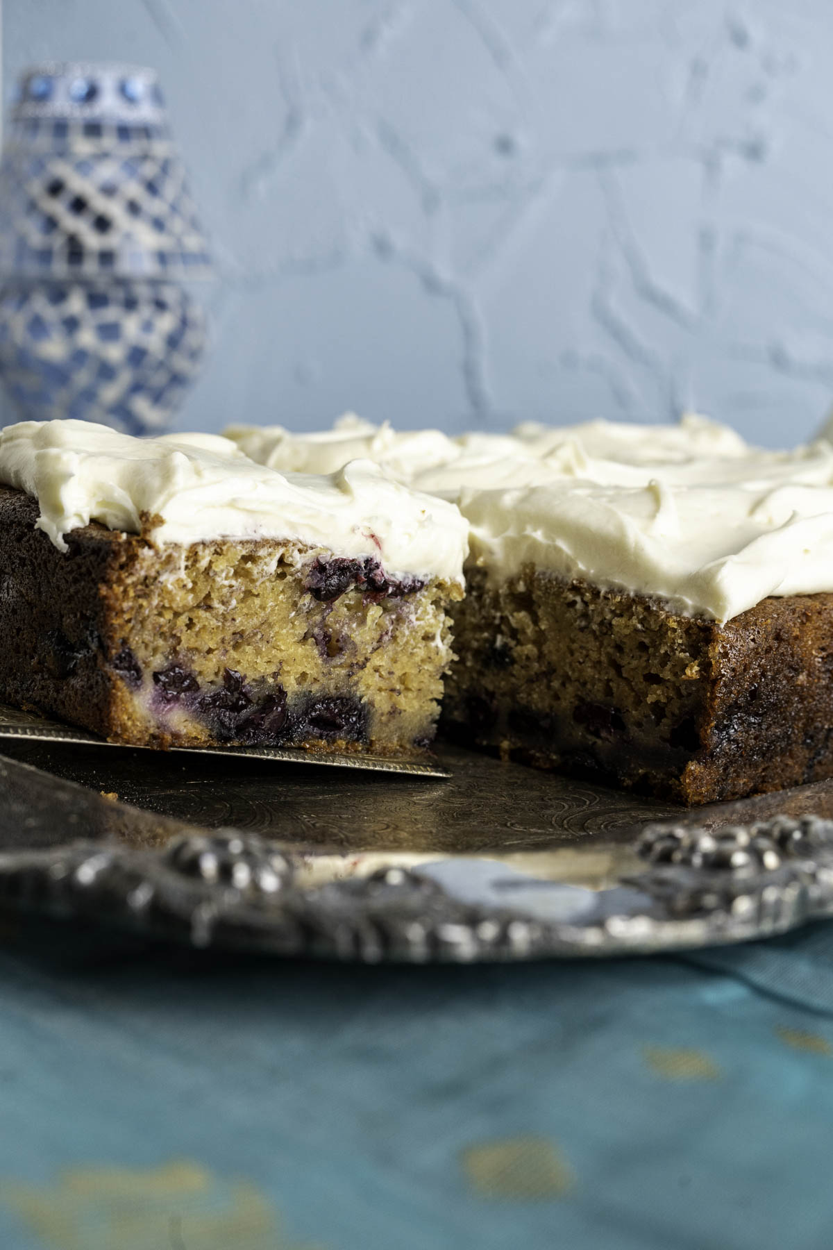 One piece of Blueberry Banana Cake in a square silver spoon showing blueberries inside.