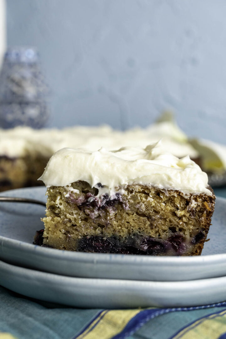 close up shot of one piece of blueberry cake with frosting in a blue plate.