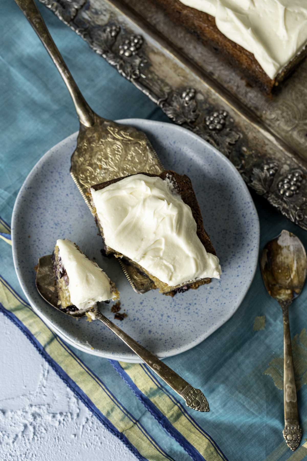 Banana cake with blueberries sitting in a golden decorative spoon on a blue plate.