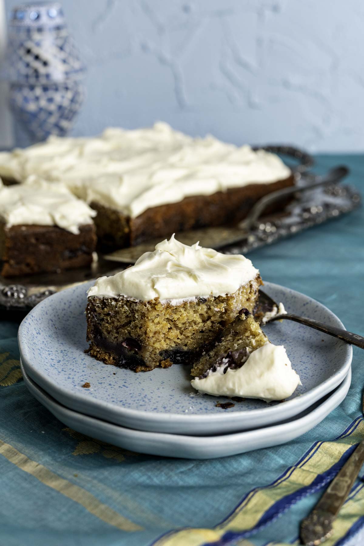 Piece of Blueberry Banana Cake in a small blue plate over a blue table cloth.