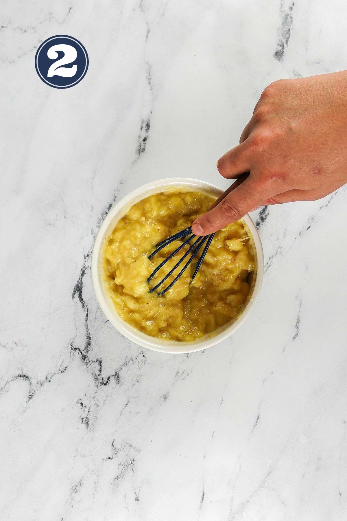 Mashing the overripe banana with a spatula in a white small bowl.