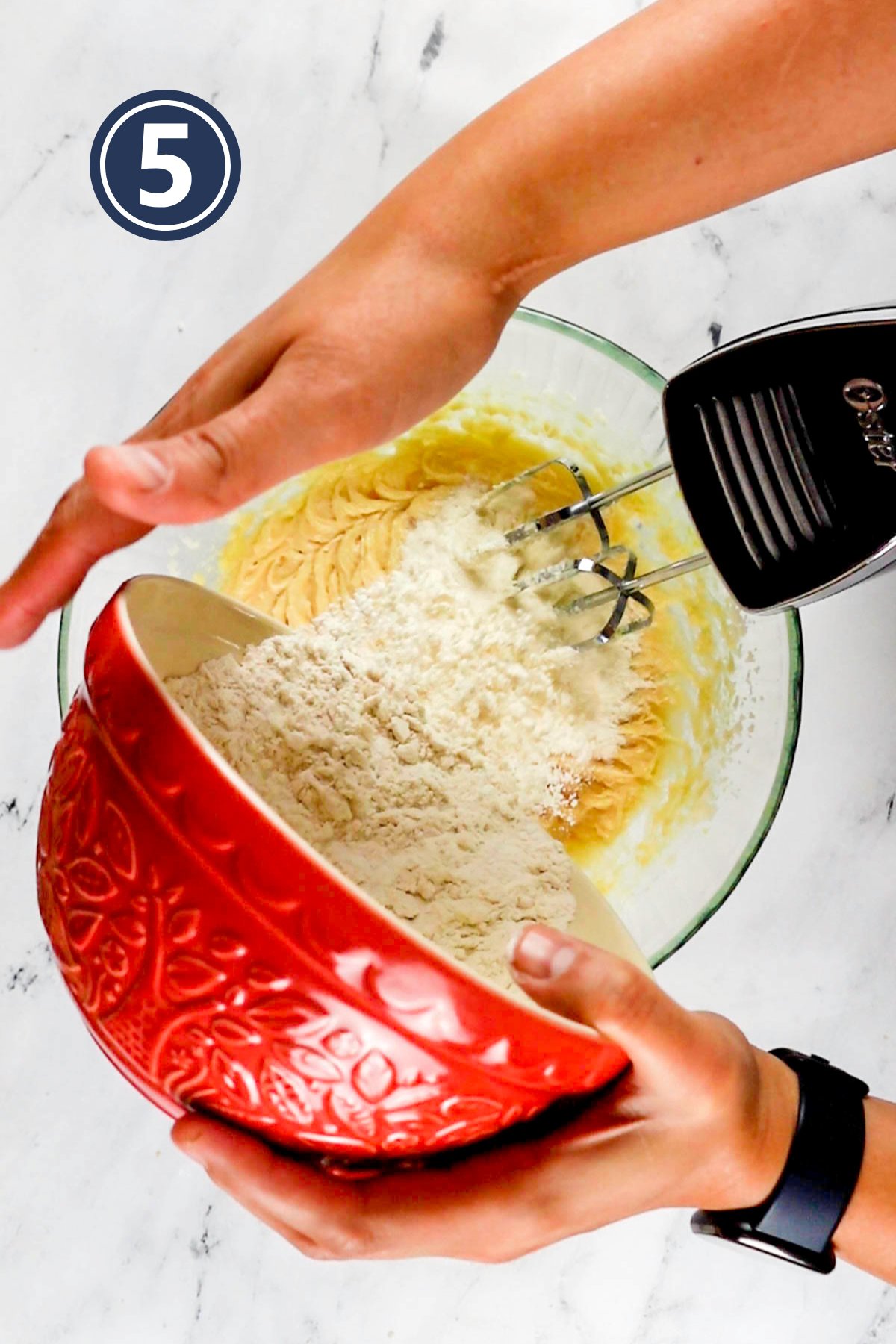 adding the dry ingredients into the wet ingredients in the mixing bowl.