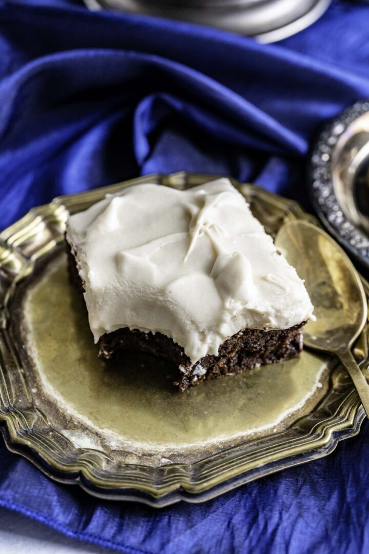 closeup shot of a bitten single shot of brownie piece with frosting on an antique golden plate.