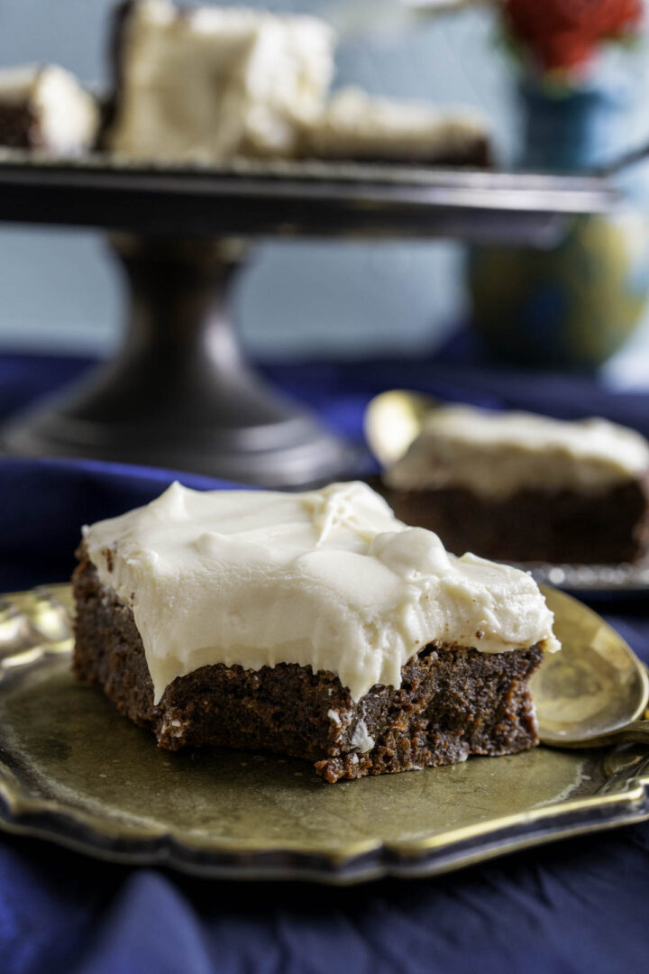 one chocolate brownie piece with cream cheese frosting on a small golden plate with a golden spoon.