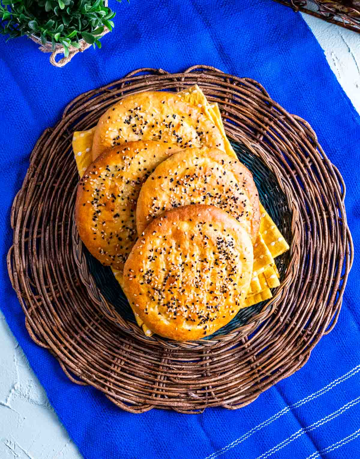 Roghni naans placed in a jute plate over a royal blue table cloth.