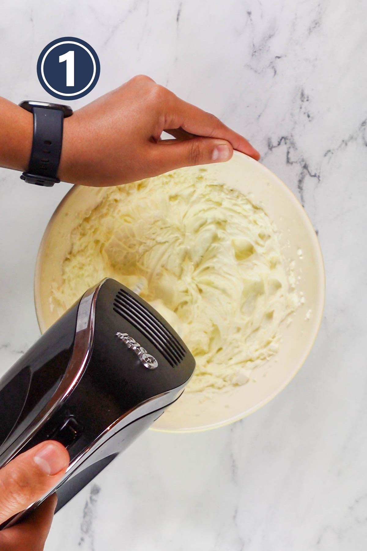 Beating butter and cream cheese using an electric mixer in a bowl.