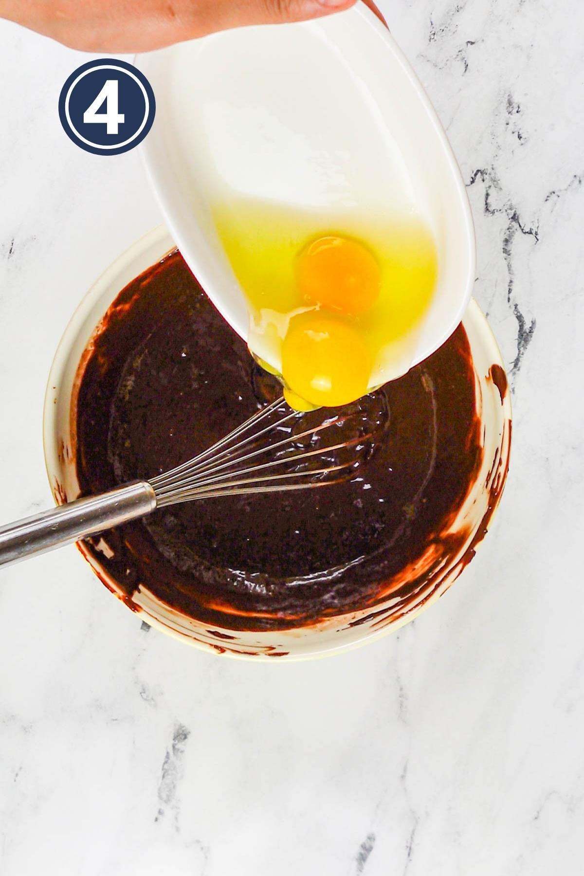 Adding in the eggs one by one in the melted chocolate and butter mixture.